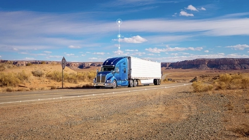 Blue Kenworth semi-truck with white trailer on a desert road with rock formations and digital signal icons